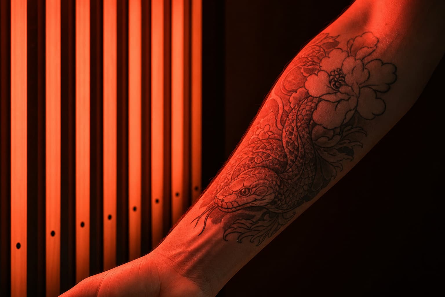 Red light therapy panel illuminating a healed tattoo on a forearm